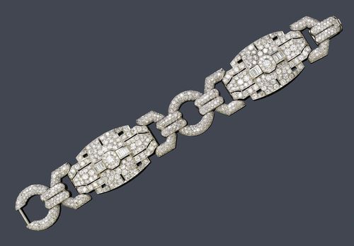 DIAMOND BRACELET, France, ca. 1930. Platinum. Fancy Art Deco bracelet of 2 geometrically designed  ornaments, each with 1 central brilliant-cut diamond, older cut, weighing ca. 0.50 ct, flanked by 6 baguette-cut diamonds weighing ca. 1.20 ct and set throughout with 134 brilliant-cut diamonds and single-cut diamonds weighing ca. 10.00 ct, connected to one another by means of 2 diamond-set ring links and eyelets with a total of ca. 400 single-cut diamonds weighing ca. 3.50 ct. W 2.7 cm, L ca. 18.5 cm.