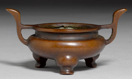 A SMALL BRONZE TRIPOD INCENSE BURNER ON CABRIOLE LEGS WITH HANDLES RISING FROM THE SHOULDER AND LIP, ZHENGDE MARK TO THE BASE.