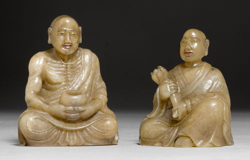 TWO ENGRAVED AND PAINTED SOAPSTONE FIGURES OF SEATED LUOHANS GRASPING AN ALMS BOWL AND A LOTUS.