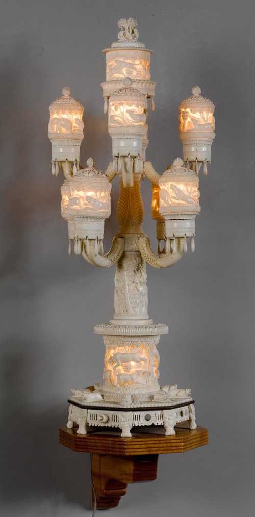 A NINE-LIGHT IVORY LAMP RICHLY CARVED WITH WILD ANIMALS, ON A WOODEN BASE.