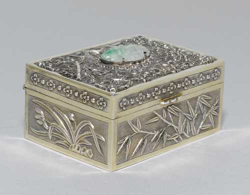 A SILVER BOX WITH A FLORAL DESIGN ON A PUNCHED GROUND AND A JADEITE MEDALLION ON THE LID.