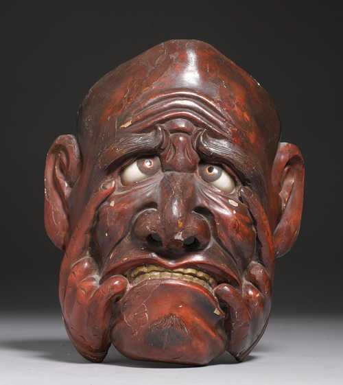 A LACQUERED WOODEN MASK OF A GRIMACING FACE. Japan, 19th/20th c. H 27 cm. The eyes inlaid with glass. Minor damage.
