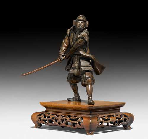 A BRONZE FIGURE OF A SAMURAI ON AN OPENWORK WOODEN STAND. Japan, Meiji Period, H 18 cm. Lacquered sword supplemented.