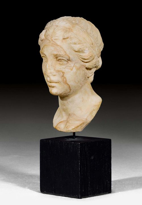 HEAD OF A WOMAN,Roman. Italy, 1st century AD. Beige marble. Fine head with braided hair and an Alice band. On a wooden base. H 11 cm (without base). H 17.5 cm (with base). Provenance: Austrian private collection, acquired in Vienna in the 1980s.