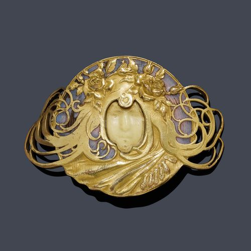 ENAMEL CLIP BROOCH, PIEL FRERES, ca. 1900. Very attractive, gold-plated Art Nouveau brooch designed as a belt clasp, decorated with 1 sculptured head of a woman with flowers between her flowing hair, the face of carved bone, the background finely enamelled in shades of lilac. Mechanical part in gold, later. Ca. 7.8 x 5.5 cm.