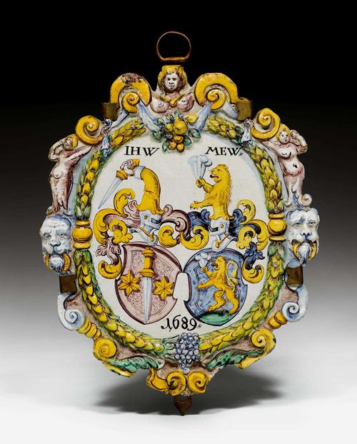 CERAMIC PLAQUE WITH ALLIANCE COATS-OF-ARMS,Winterthur, dated 1689. Workshop Pfau. Oval, tiled stove plaque modelled with festoons, winged genies and lion heads above a laurel wreath, with two Swiss family coats-of-arms: 'IHW' and 'MEW', dated 1689. H 36 cm.