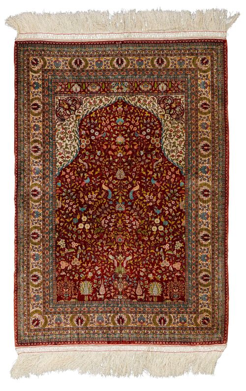 HEREKE SILK PRAYER.Fineness: 18x18 knots/cm2. Red mihrab with beige spandrels, finely patterned with trailing flowers and animals in harmonious colours, white border with blossoms and palmettes, in good condition, 72x102cm.