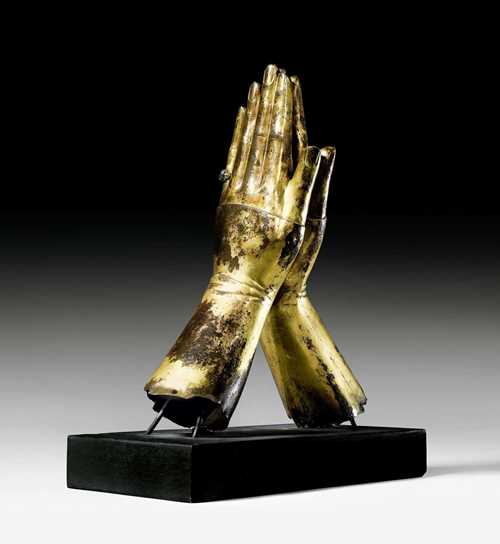 PLEADING HANDS,fragment of a so-called "figure gisante", Renaissance, Limoges, 14th century. Gilt copper. The arms covered with buttoned gloves. The left small finger with ring with green stone. The gilding rubbed. Mounted on an ebonized wooden base. H 31.5 cm. Provenance: - Traditionally considered to be from the former Robert Kahn-Sriber collection, Paris. - From an important collection. With expertise by Prof. Dr. G. Freuler, Zurich, 27.8.1998. With material analysis by Dr. P. Northover, University of Oxford, #R811. With second material report by Aventis, Research & Technologies, 29.7.1998. The hands offered here are in the licentiate thesis by Ms. K. Holderegger, under Professor Dr. N. Gramaccini at the University of Berne 1998, described in detail and set in the historical context of the "figures gisantes".