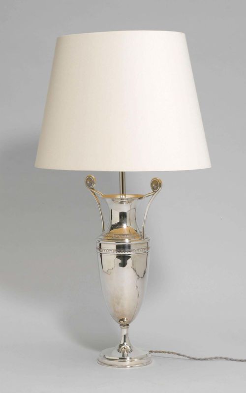 PAIR OF TABLE LAMPS,Empire style. Metal, silver-plated. Designed as a vase with small handles and palmette decoration. Light beige fabric shade. H 70 cm. Fitted for electricity.