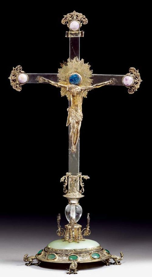 CRUCIFIX,Early Baroque, probably German, 17/18th century Rock crystal, silver, amethyst, agate and green and blue gems. With aureole, dragon, saints, scrolls and frieze, on plinth with dragon-shaped feet. H 54 cm.