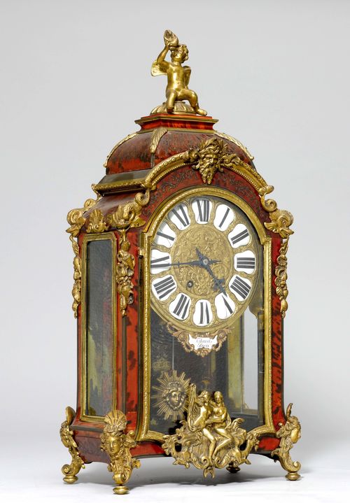MANTEL CLOCK, in the style of Louis XIV, France, signed THUREL À PARIS. Glass-covered case with boulle marquetry in red tortoise shell and brass. Bronze mounts designed as espagnolettes, dolphins and flowers. Figure of Cupid on top. Dial in relief with enamel cartouches. Movement with anchor escapement striking the half-hours on gong. H 59 cm. Provenance: Gut Aabach, Risch am Zugersee.