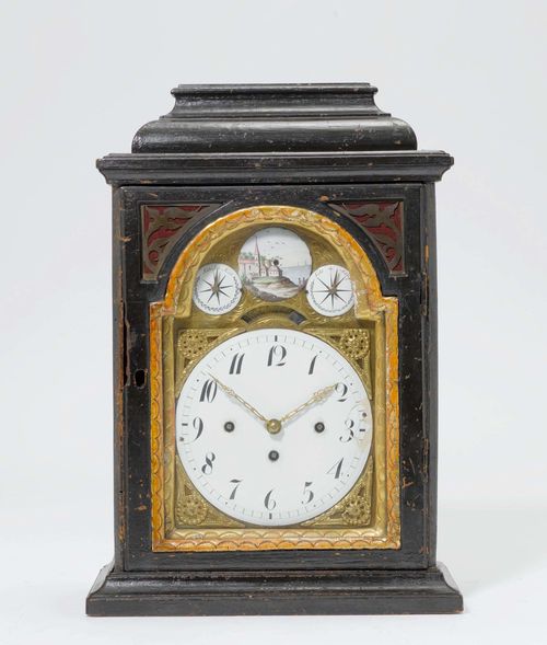 CLOCK, Baroque, Southern Germany or Austria, 18th century. Blackened wood, partial gilt. Brass, engraved fronton with white enamel dial and 3 small enamel plates, 1 with a view of a village on the water and 2 auxiliary dials for the striking mechanism. Verge escapement, and 4/4-hour strike on 2 bells (can be turned off). H 43 cm. Some losses, dial with repairs.