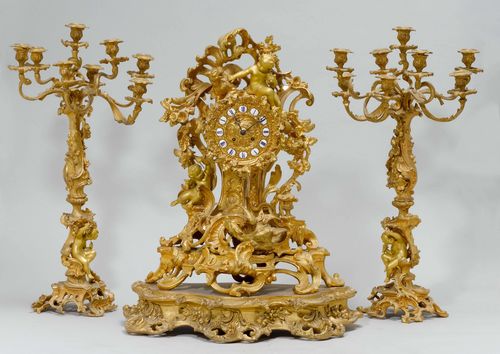 MANTEL SET, Napoléon III, France. Bronze, parcel-gilt. Comprising: clock and 2 candelabras. Open-worked design with rocailles, dragons, putti and flowers. Dial in relief with enamel cartouches. Parisian movement striking the 1/2-hour on bell. H without wooden plinth 60 cm. The candelabras with 8 curved light branches on a baluster shaft and with an open-worked base. H 72 cm.