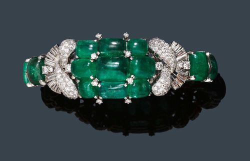 EMERALD AND DIAMOND BRACELET, ca. 1935. Platinum. Fancy bracelet, set throughout with 13 graduated emerald cabochons, between 24 baguette-cut diamonds. The broader top is set with 9 emerald cabochons, flanked by four stylised, pavé-set leaf motifs and two fan-shaped attaches set with diamonds. Total weight of the emeralds ca. 38.00 ct. Total weight of the 40 baguette-cut diamonds ca. 1.50 and total weight of the ca. 118 brilliant-cut diamonds ca. 2.50 ct. Clasp in white gold. L ca. 20.5 cm. With case.