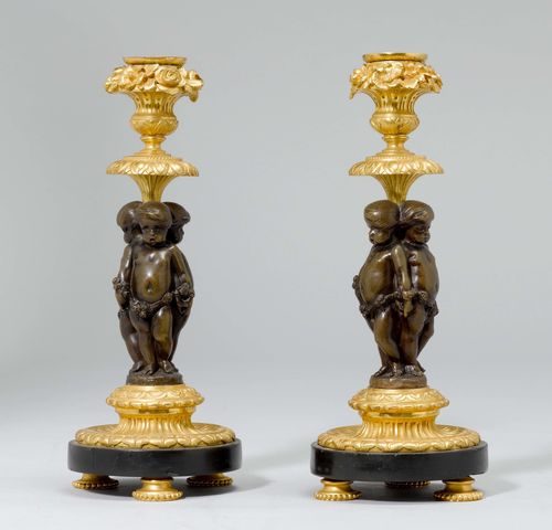 PAIR OF CANDLESTICKS,in the style of Louis XVI, France. Bronze, parcel-gilt. Shaft designed das 3 putti, vase-shaped nozzle. Floral wreath all around. On a round plinth with gadrooned decoration. H 24.5 cm. Provenance: Gut Aabach, Risch am Zugersee.