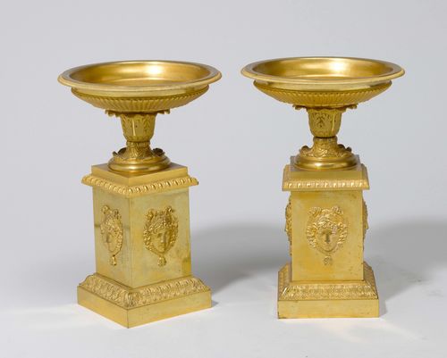 PAIR OF BOWLS,Restoration, France. Gilt brass. Flat, round bowl on a retracted foot and square plinth. The walls gadrooned and decorated with palmettes and faces. H 28 cm.