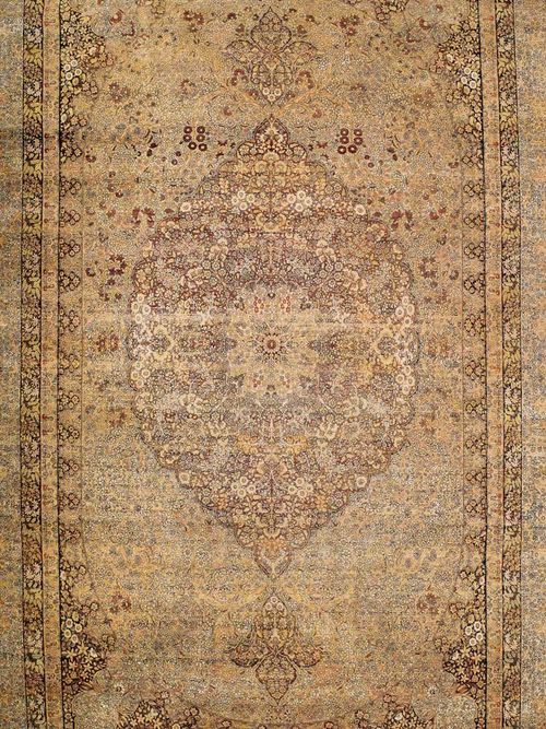 KIRMAN antique, signed.Floral central medallion on a beige ground with black corner motifs, the entire carpet is finely patterned with floral motifs in attractive pastel colours, border in white and black, signs of wear, otherwise in good condition, 635x390 cm.