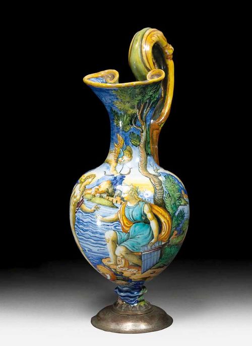 MAIOLICA JUG: 'BROCCA', probably Urbino second half of the 16th century.In the style of Antonio Patanazzi or Fontana workshop. Decorated with lion paws and grotesque mask. Painted with a mythological scene with Cupid shooting an arrow towards Pan and Venus. The foot replaced with a metal mount. H 31cm. Repair to the handle