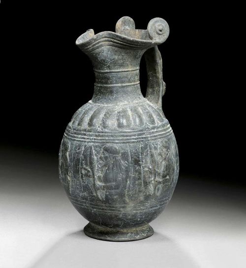 JUG, known as a "Bucchero Pesante-Kanne",Etruscan, 2nd half of the 6th century BC Dark painted fired clay. With figural handle. The sides with fine relief depiction of an armed soldier. H 34.5 cm. Provenance: - Galerie Arete, Zürich. - from a French private collection, acquired in 1972.