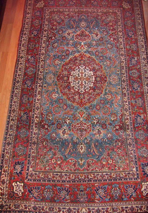 ISFAHAN old.Blue central field with a red central medallion and corner motifs, patterned with trailing flowers and palmettes, red border, signs of wear, fringes replaced, 250x140 cm.