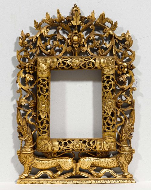 A GILT WOOD MIRROR FRAME RICHLY CARVED WITH FOLIAGE AND BLOSSOMS EMANATING FROM TWO OPPOSED LIONS. Thailand, 54x35.5 cm.