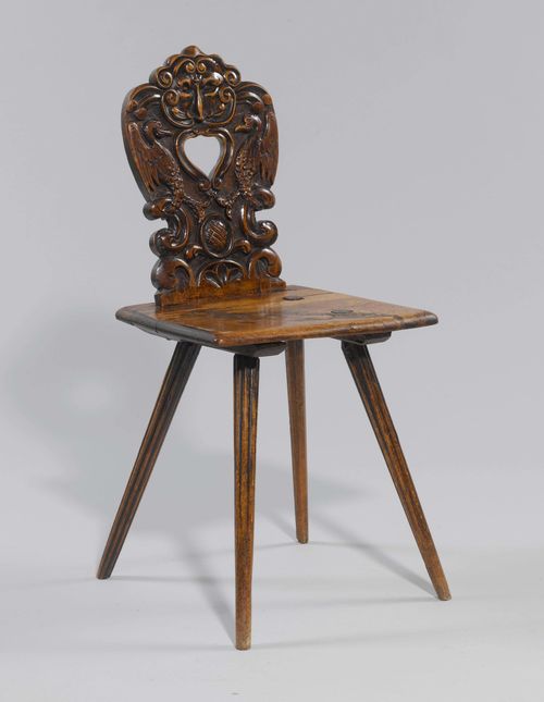 STABELLE WITH GROTESQUE FACE, in theRenaissance style, Switzerland. Beech and walnut, carved with mask, birds and volutes. Trapezoid seat with inclined legs. Curved backrest with heart-shaped, pierced handle.