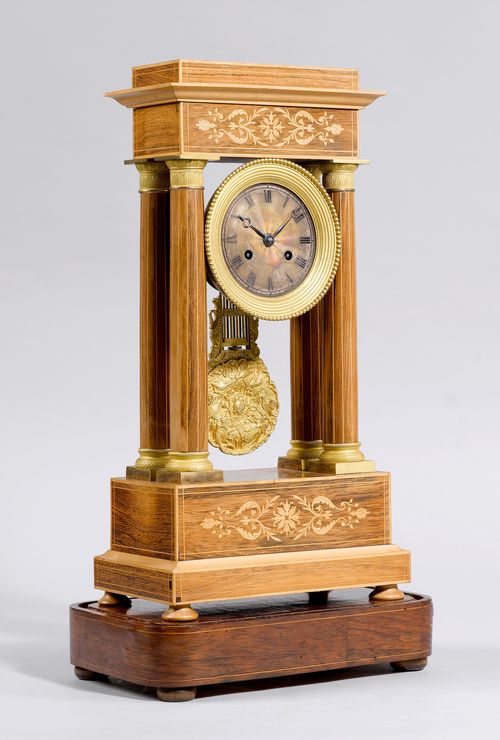 PORTAL CLOCK,Charles X, France. Rosewood, inlaid with fillets and fleurons. Architecturally-shaped case on a square base with spherical feet. Metal dial with remains of silver plating, gilt bronze lunette. Parisian movement, striking the 1/2-hour on bell. H 48 cm. Additional wooden plinth and glass cloche. Striking mechanism requires servicing.