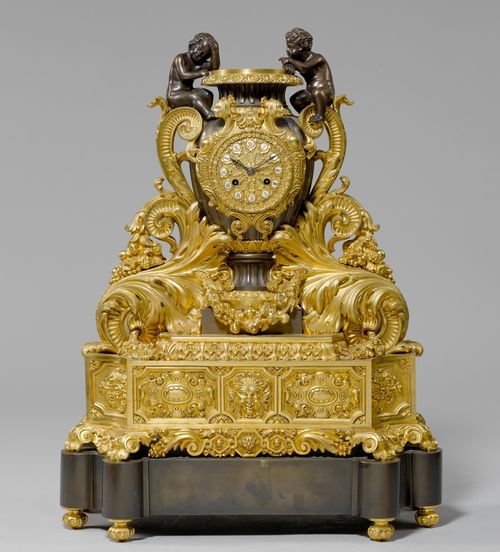 IMPORTANT CLOCK "AUX AMOURS",Napoleon III, Paris. Gilt bronze, in part burnished. Designed as a vase with handles and decorated with 2 putti seated, on an opulently decorated, stepped rectangular base with spherical feet. Bronze dial. Parisian movement striking the 1/2-hour on bell. H 61 cm. Bell and pendulum missing.