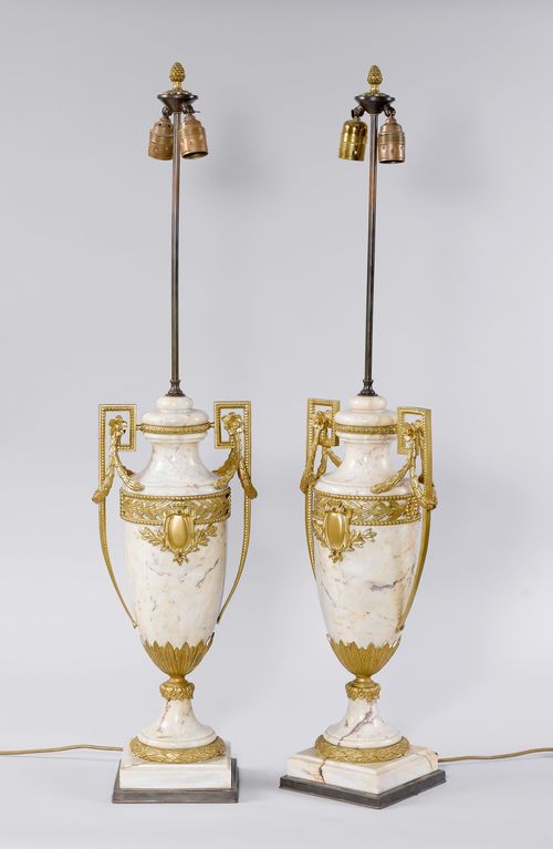 PAIR OF LAMPS AS VASES,ca. 1900. Off-white marble. Amphora-shaped, with a retracted neck and a round foot, on a square plinth. Bronze mounts with decorative frieze and garlands. Fitted for electricity. H 95 cm.
