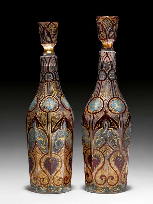 2 CARAFES WITH ARABESQUE DECORATION, probably Bohemian, 19th century. Faceted glass, painted with enamel colours, with stylised tendrils and decorations in ruby red, powder blue and accentuated with gold. H 31 cm. (4)