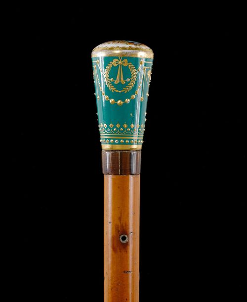 WALKING STICK WITH PORCELAIN GRIP,18th century. Conical grip depicting a minstrel with a lady, decorated with gold on a green ground. Malacca wood stick. L 94 cm.