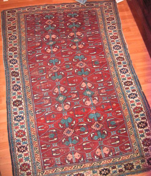 SHIRVAN antique. Honeycomb patterned, dark red central field with stylised plant motifs in pink and blue, white border, strong signs of wear, 210x140 cm.