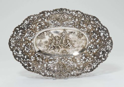 OVAL BASKET,Germany, after 1888. Oval with curved edge. Open-worked walls all around and decorated with floral ribbons. On the longitudinal side: two hearts with scenic depictions of putti. Matching scene in the mirror. L 39 cm, 660 g.