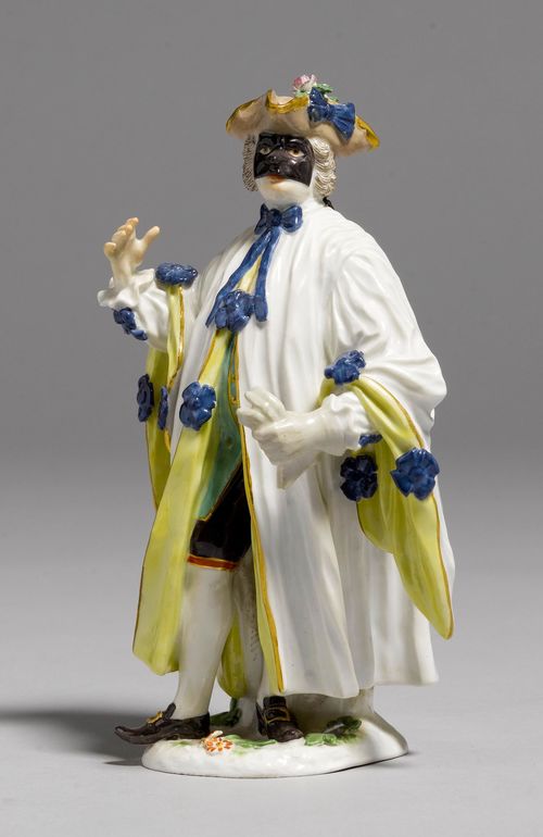 FIGURE OF "AVOCATO",Meissen, from a series of the Commedia dell'Arte, ca. 1921-1934. Wearing a black mask, a leather-colour tricorn, a white cloak with yellow lining and blue bows over a green vest and black knickerbockers. Underglaze blue sword mark with dot, model number 942. incised, press number. H 15,5 cm.