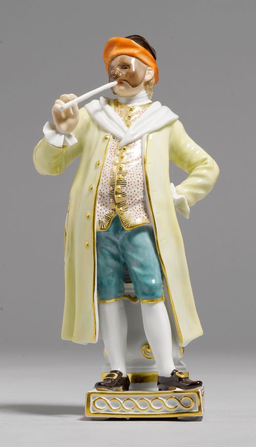 COMEDY FIGURE, CORTESAN,Meissen, after 1948. Smoking a pipe, the face covered by a mask  and wearing a black, red-lined hat, a yellow coat and green knickerbockers. Underglaze blue sword mark, model number impressed 64559, additional press number. H 17.5 cm. Tip of the pipe broken.