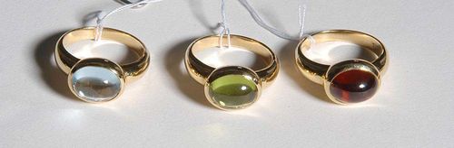 THREE GEMSTONE RINGS. Yellow gold 750. A set of 3 fashionable rings, the top set with 1 oval peridot cabochon of ca. 2.80 ct and 1 garnet cabochon of ca. 3.00 ct and 1 treated topaz cabochon of ca. 2.80 ct respectively, in a casual pronged setting. Size 51.
