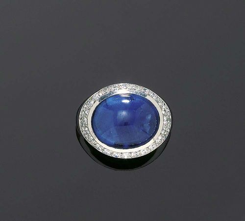SAPPHIRE AND DIAMOND RING. White gold 750. Modern mantle ring, set with 1 oval sapphire cabochon of ca. 15.00 ct flanked by 33 brilliant-cut diamonds totaling 0.70 ct. Size 52.