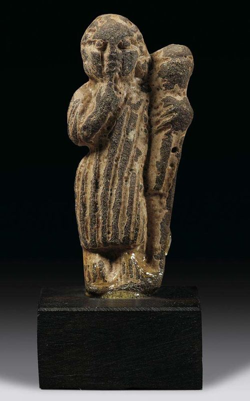 AMULETT OF A GODDESS WITH CORNUCOPIA, probably Roman, 2.-4 century AD Grey stone. Mounted on wooden plinth. H 3.5 cm.