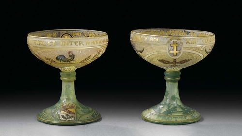 Two small shooting cup, Daum, dated 1906. Colourless glass with yellow inclusions, etched and enamelled with thistle decoration, cockerel, eagle and coat of arms, finely worked in gold, the rim inscribed : XIII. Concours National Et International De Tir. Nancy 1906, foot with inscription: Qui s'y frotte s'y pique. One cup repaired, H. 11.5 cm.