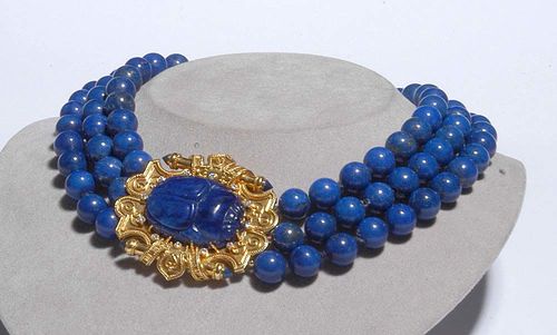 LAPIS-LAZULI, GOLD AND DIAMOND NECKLACE, ca. 1950. Yellow gold 750. Three-row necklace made of fine lapis-lazuli spheres of ca. 11 mm Ø. Ornamental fastener set with 1 large, carved lapis-lazuli scarab and decorated with knurled gold wires and 12 additional brilliant-cut diamonds, totalling ca. 0.20 ct. L ca. 40 cm.