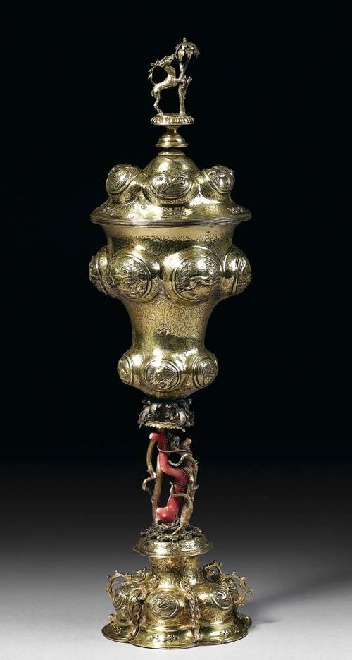 SILVER-GILT CUP AND COVER, probably Augsburg circa 1650. With maker's mark. The foot with hunting motifs and animals' heads, the shaft with twisted branches and red coral (coral damaged) the cup with animal motifs and finely engraved ground, corresponding cover. H 35.5 cm, 510 g.