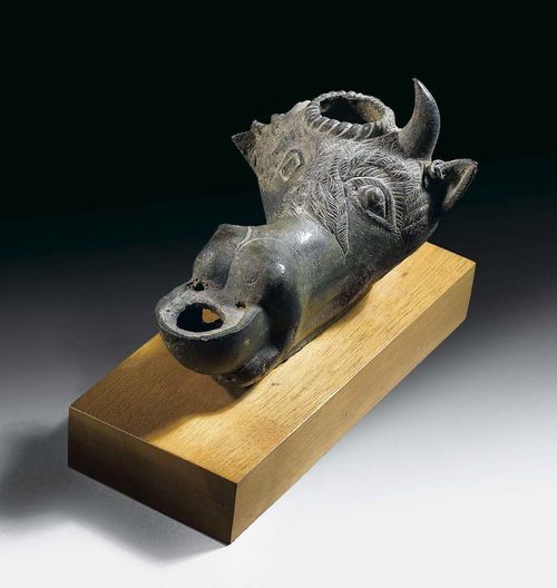 OIL LAMP IN THE FORM OF A BULL'S HEAD Sicily, 3. century BC. Bronze. One eye with silver inlay, one cheek missing. Mounted on wooden plinth. L 10 cm. Provenance: - Collection of Baron Gindici, Agrigento. - Private collection, Zurich, acquired from Donati, Lugano.