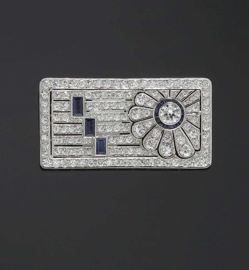 DIAMOND AND SAPPHIRE BROOCH, circa 1925. Platinum. Floral and geometric pierced brooch. The flower motif set with 1 old-cut diamond of ca. 0.75 ct, surrounded by small sapphire carrés, also 29 old cut diamonds. The brooch also set with 117 old cut diamonds and 3 sapphire baguettes. Total weight of diamonds ca. 6.20 ct, of sapphires ca. 1.40 ct. White gold pin.