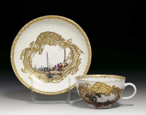 CUP AND SAUCER, Meissen, circa 1745. Painted with a Kauffahrteiscene and landscape setting with figures in gilt lattice work cartouches picked out in black, the interior of the cup with a landscape scene in purple camaïeu, crossed swords in underglaze-blue, gilt numeral 39 to both pieces, small chip to saucer, gilding slightly rubbed.