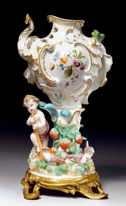 POT POURRI 'THE SEASONS', Meissen, circa 1750.Mounted on a gilt bronze foot. The openwork rocaille decorated form heightened in gold and painted with a reserve on the front enclosing a bouquet of vegetables, set on a similarly modelled rocky plinth with applied palm leaves and strawberry plants, to the left a boy and hens on the plinth. Underglaze blue sword mark. H 27cm. The lid missing. Somewhat restored.