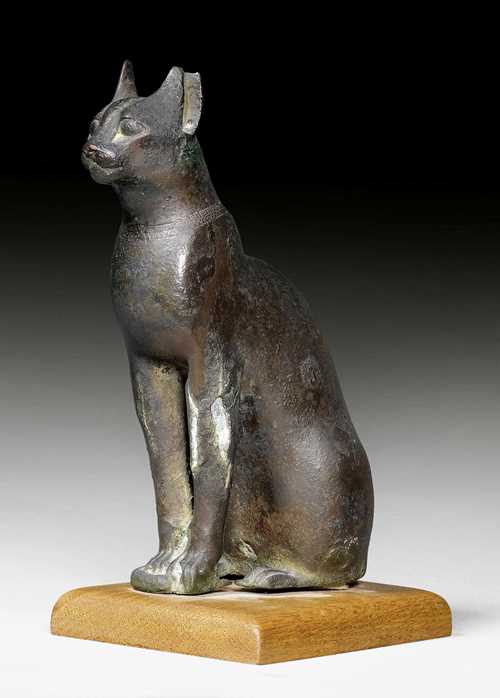 BRONZE FIGURE OF A CAT,Egyptian Late Period, 26th Dynasty, 650-500 BC. Bronze, hollow cast with remains of cuprite and old collection patina. On a wooden base. Some losses. H 22 cm.