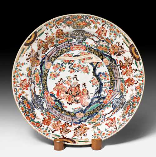 A LARGE IMARI BOWL WITH LADIES IN A GARDEN SCENE. Japan, Arita, Meiji Period, D 51 cm. Wooden stand. Old clamp restorations.