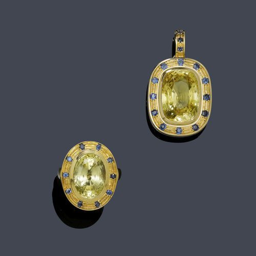 SAPPHIRE PENDANT AND RING. Yellow gold 585, 37g. Decorative pendant, set with 1 antique-oval, yellow sapphire weighing ca. 28.00 ct, the setting and the clip eyelet additionally decorated with 15 blue sapphires weighing ca. 0.50 ct. Matching ring, set with 1 oval, yellow sapphire weighing ca. 15.00 ct and decorated with 10 blue sapphires weighing ca. 0.30 ct. Size ca. 63. With copy of insurance estimate.