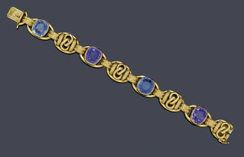 SAPPHIRE AND GOLD BRACELET AND RING, ca. 1950. Yellow gold 750. Decorative bracelet of 4 elliptical links, set with 2 light blue and 2 violet antique-oval Ceylon sapphires weighing ca. 25.00 ct in total, unheated, as well as 4 elliptical links with knot motifs and textured ornaments. L ca. 19 cm. Matching ring set with 1 sapphire weighing ca. 10.50 ct within a border of 6 brilliant-cut diamonds weighing ca. 0.20 ct in total. Size ca. 52, with size adjustment insert.