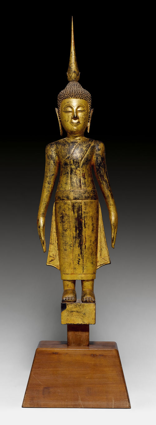 A WOOD AND GOLD-OVER-BLACK LACQUER FIGURE OF A STANDING BUDDHA ON A WOODEN BASE.